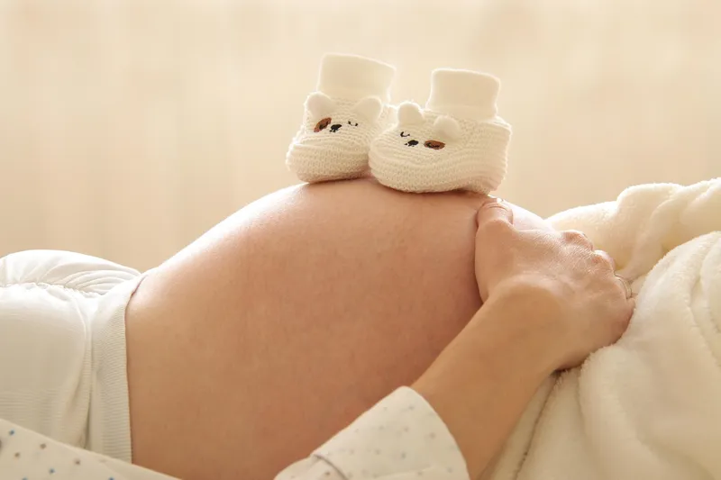 Tiny baby shoes next to pregnant belly